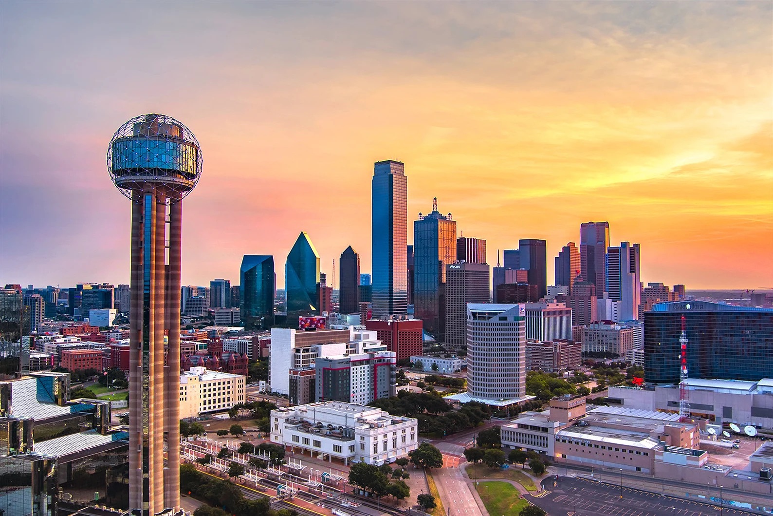 Dallas city skyline at sunset with the Reunion Tower prominently visible on the left.