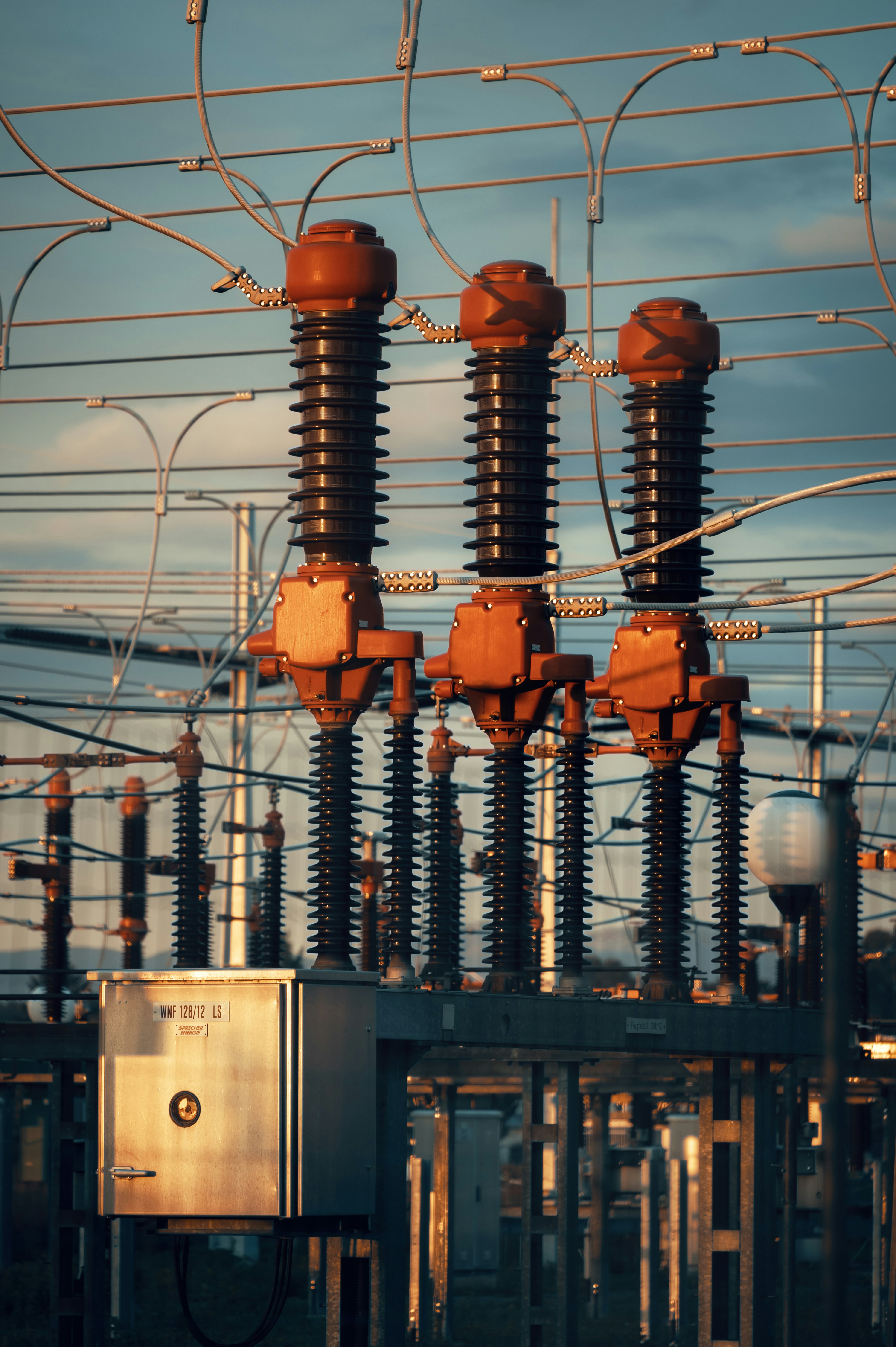 Close-up of high voltage electrical insulators and wiring in a power substation at sunset.