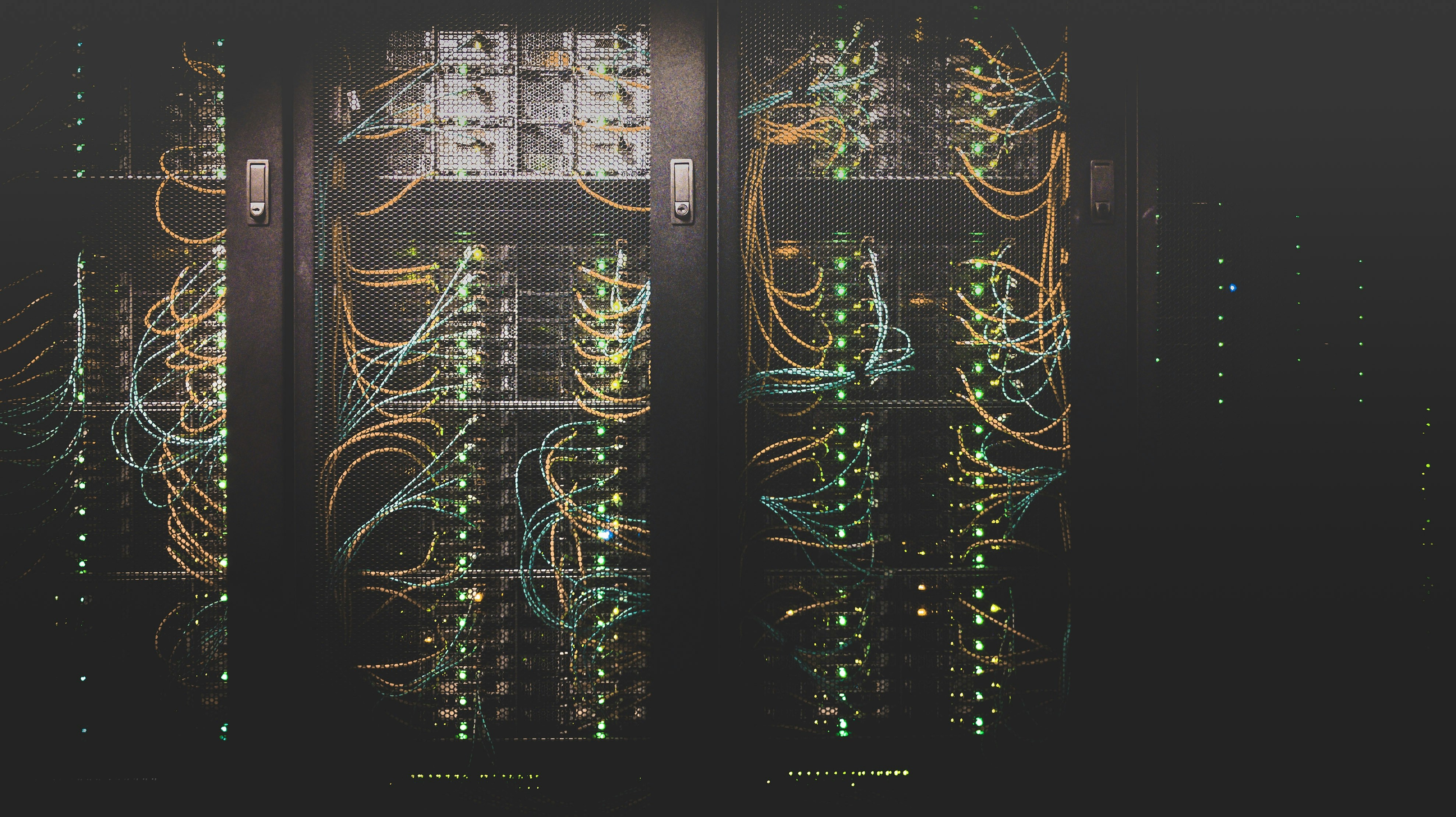 Server racks with numerous illuminated network cables and blinking green and blue indicator lights behind a mesh door.