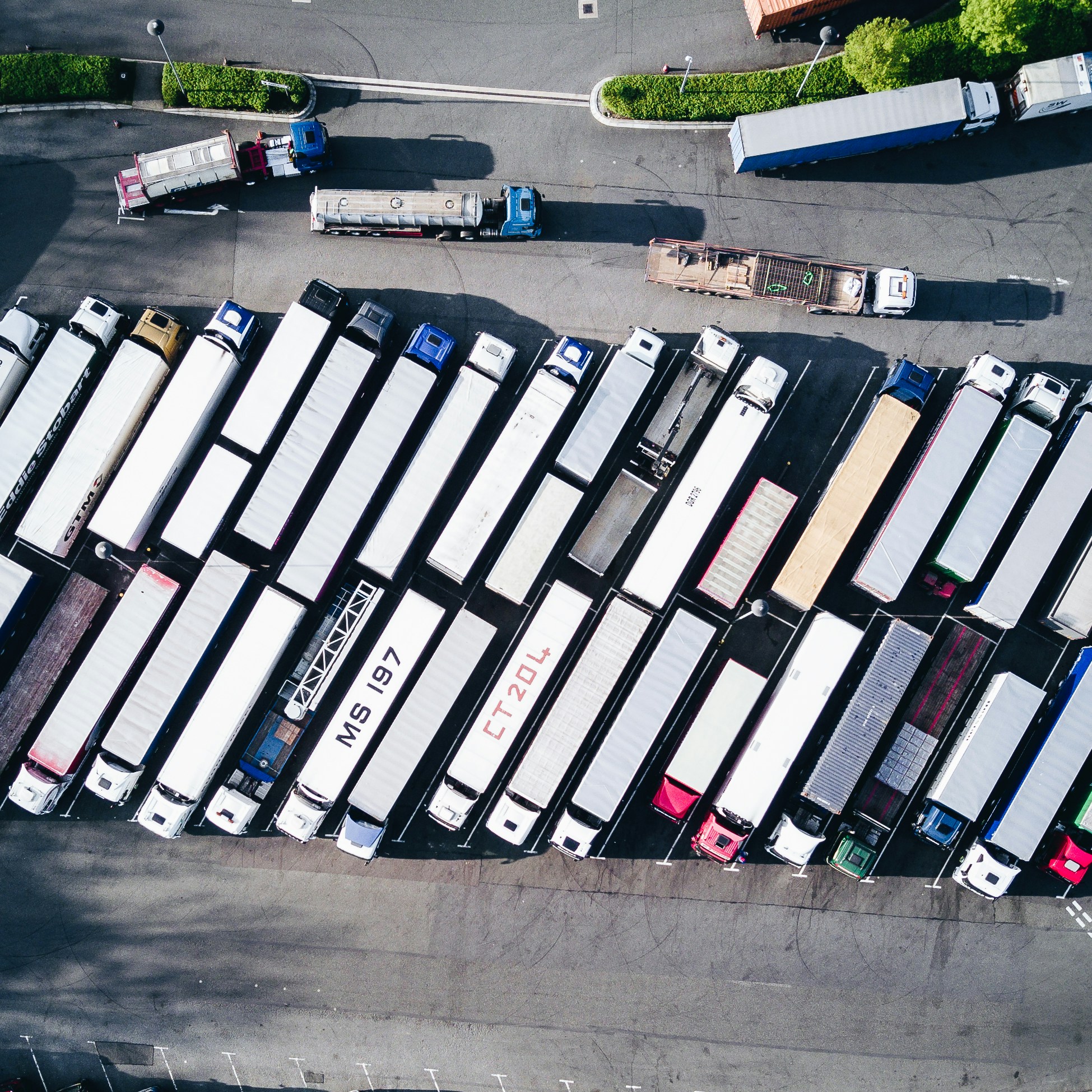 Aerial view of a parking lot filled with multiple parked semi-trailer trucks arranged in rows.