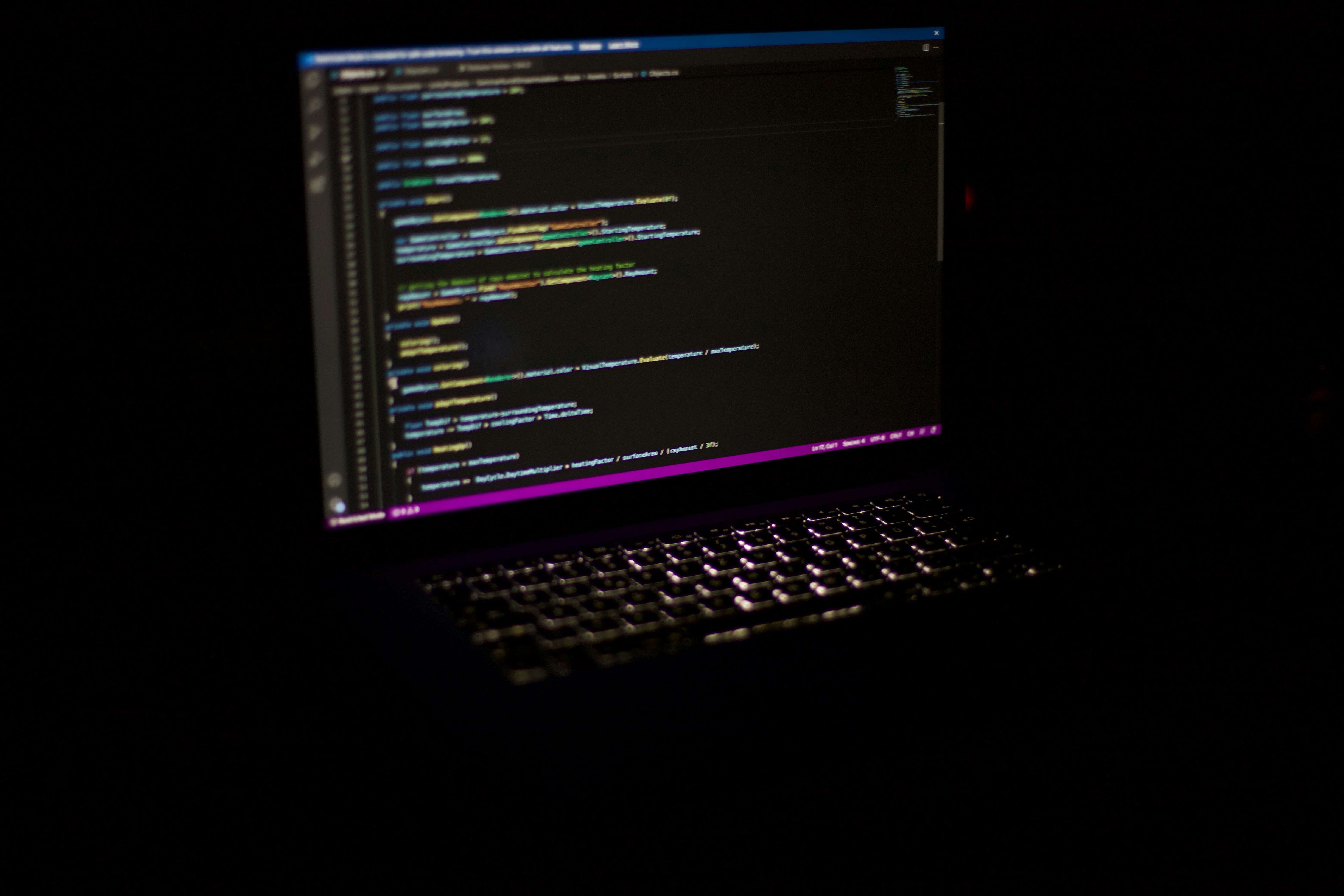 Dimly lit laptop displaying colorful code in a programming editor with a glowing keyboard.