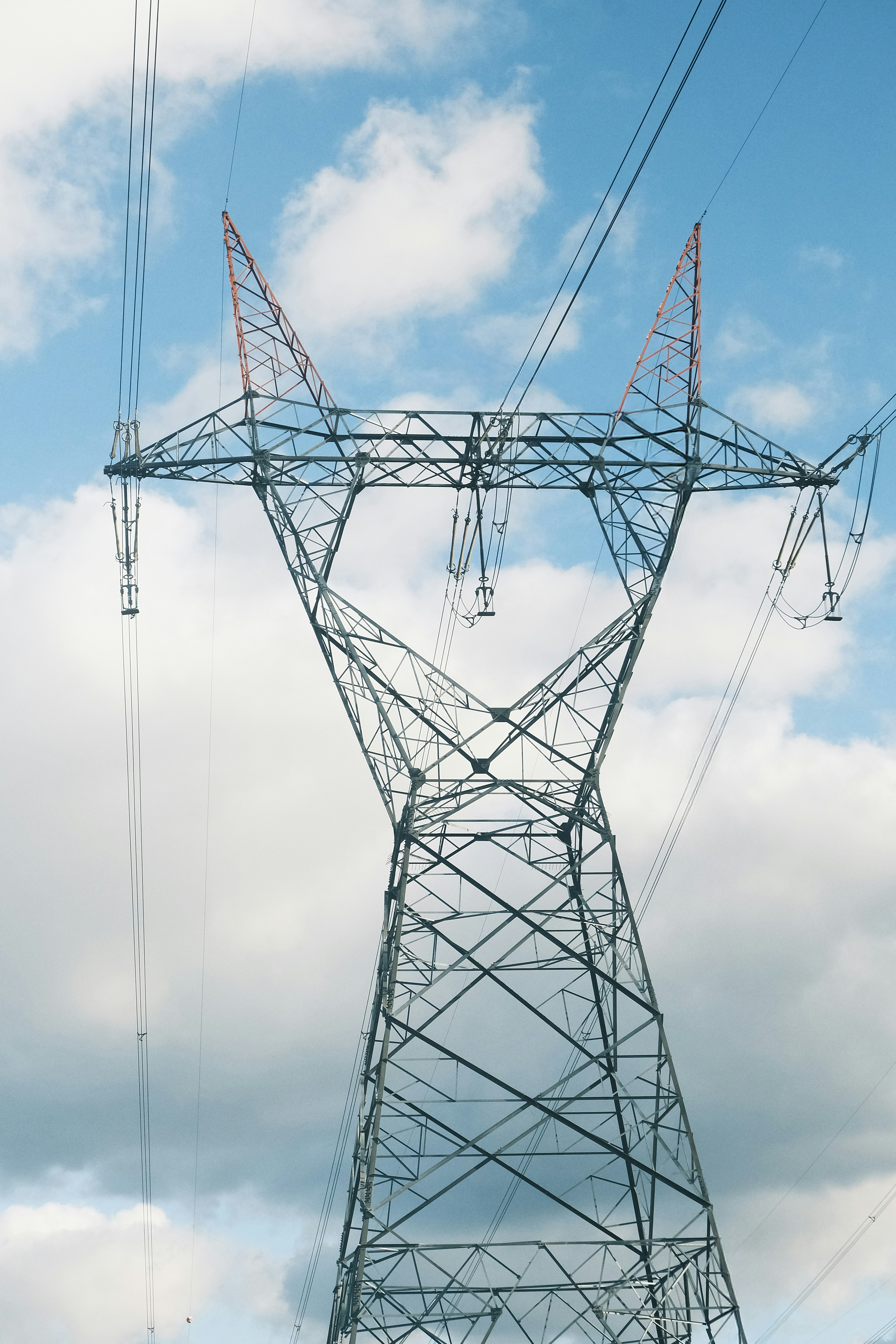 High-voltage electricity transmission tower against a blue sky with clouds.