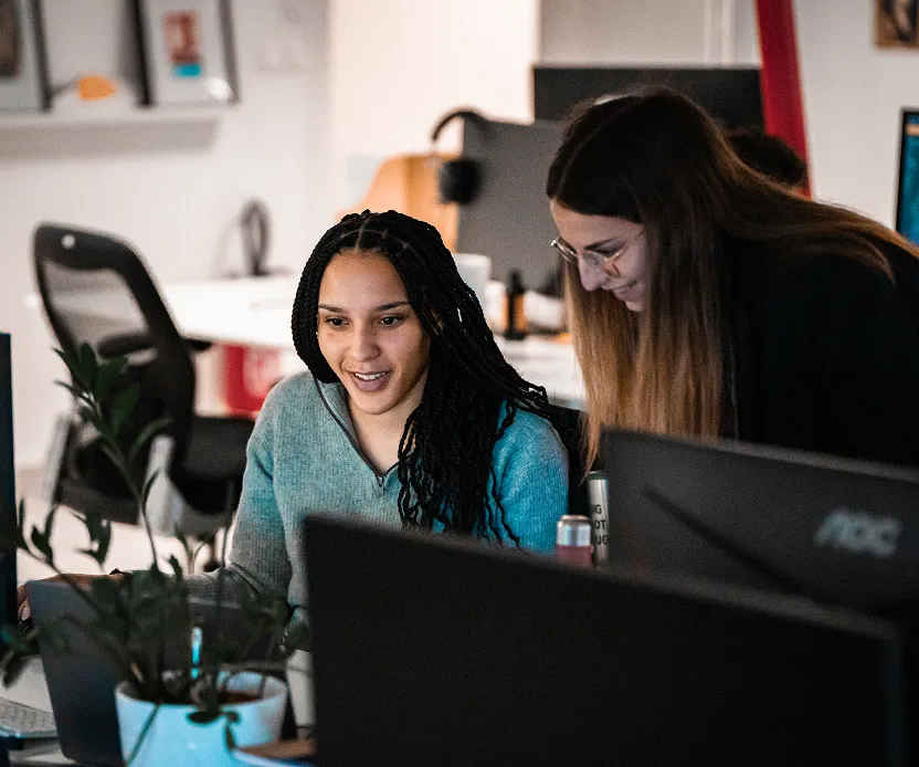 Groupe de cinq personnes assises autour d'une table en bois dans une salle sombre, regardant un grand écran d'ordinateur.