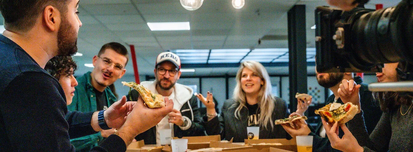 Un groupe de personnes souriantes partageant des parts de pizza autour d'une table avec des gobelets en plastique.