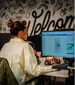 Groupe de cinq personnes assises autour d'une table en bois dans une salle sombre, regardant un grand écran d'ordinateur.