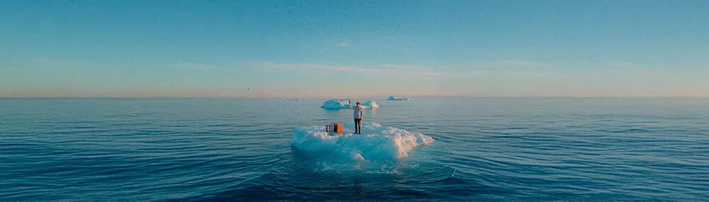 Personne debout sur un iceberg au milieu de l'océan, tenant un appareil photo vers le ciel bleu.
