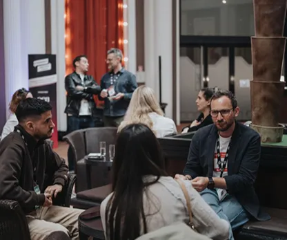 Groupe de personnes discutant autour de tables basses dans un espace intérieur confortable.