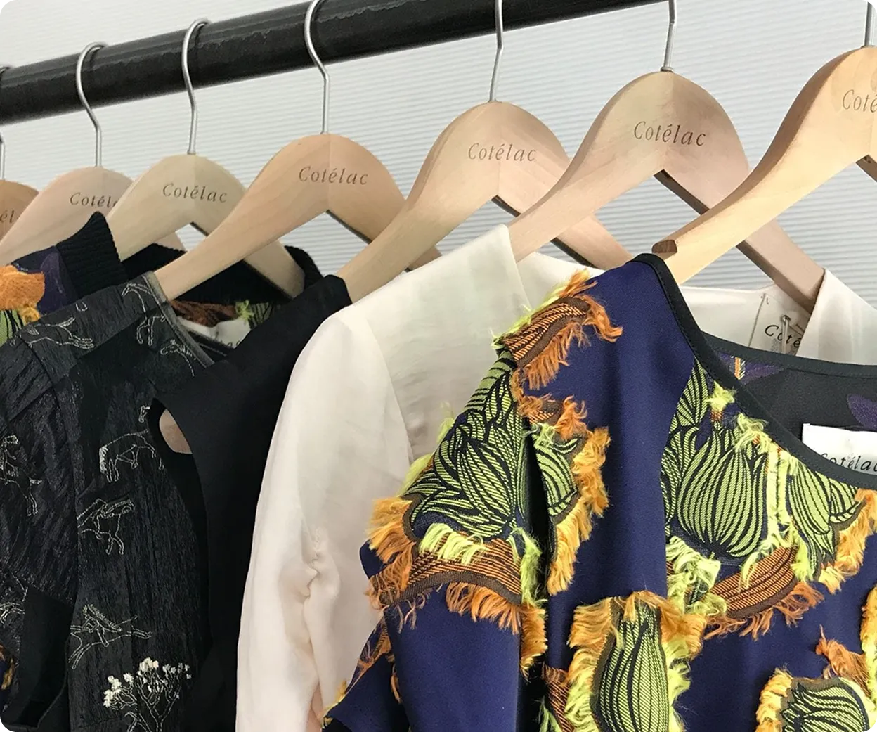 Plusieurs vêtements sur des cintres en bois portant la marque Cotélac, dont un vêtement bleu avec motif floral vert et détails orange.