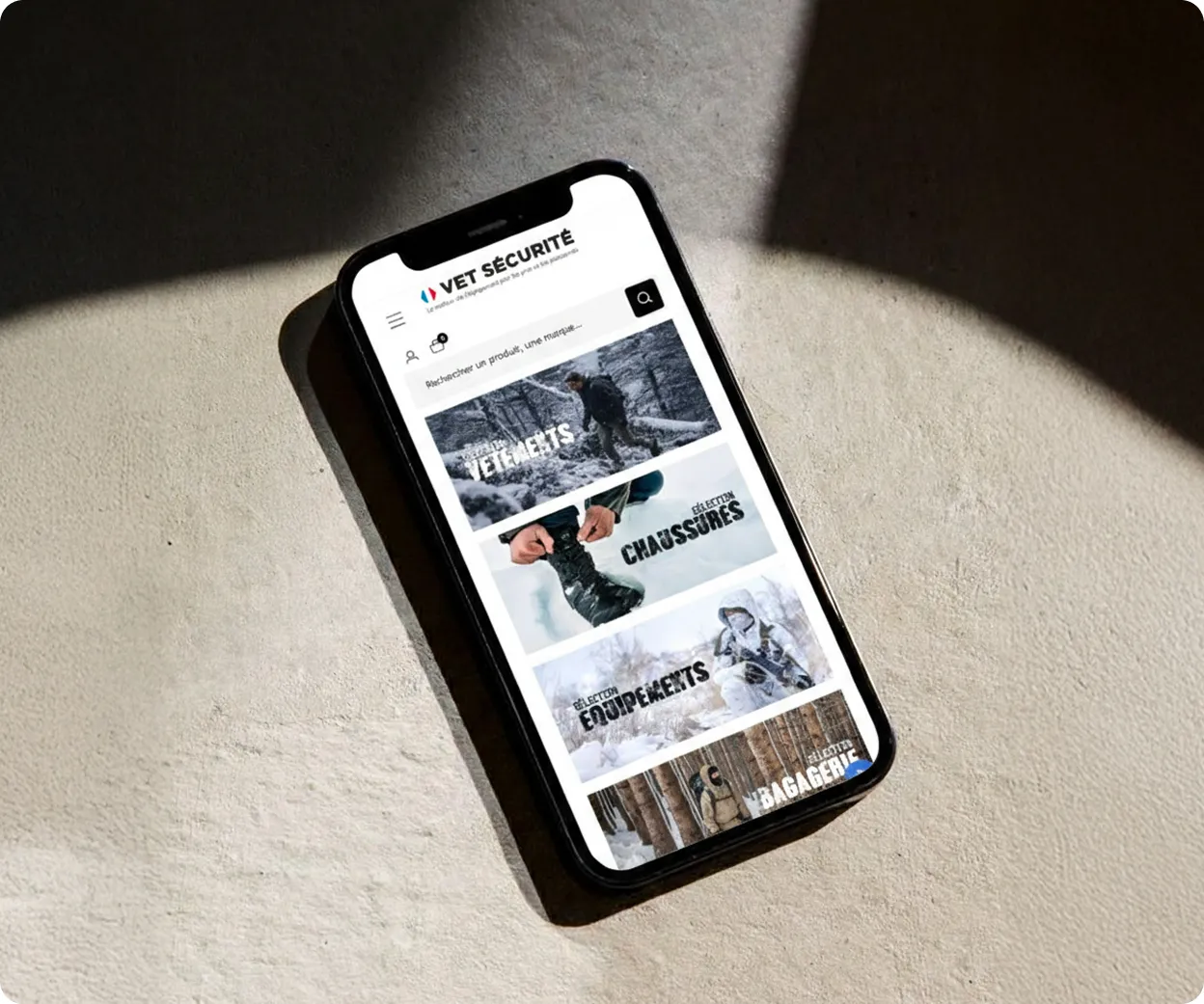 Smartphone affichant le site Vet Sécurité avec des catégories de produits : vêtements, chaussures, équipements et bagages.