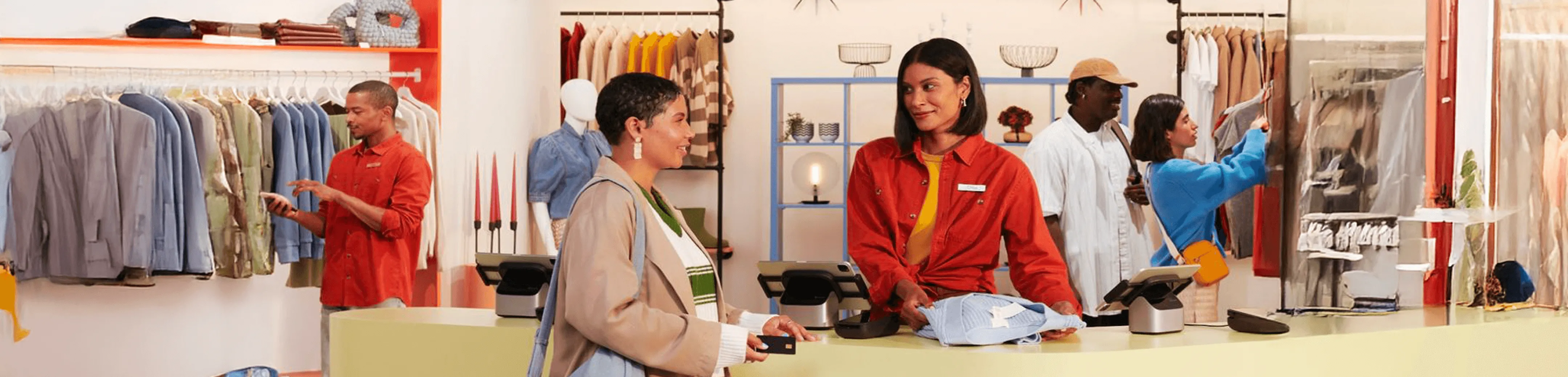 Client achetant des vêtements dans un magasin avec une vendeuse à la caisse et d'autres clients consultant des articles sur des portants.