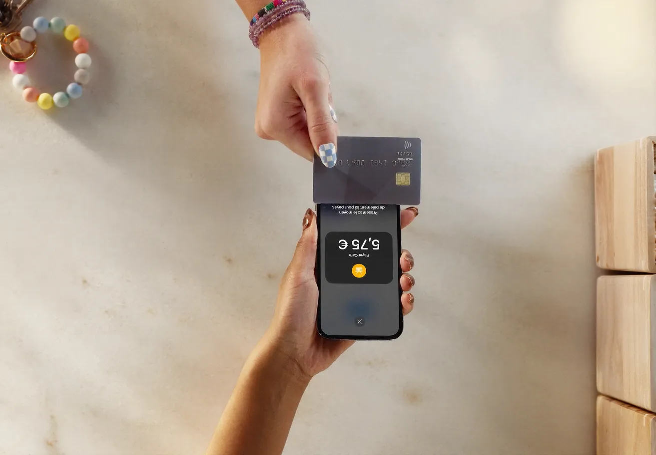 Une main insère une carte de paiement sans contact dans un smartphone tenu par une autre main, affichant un montant de 5,75 €.
