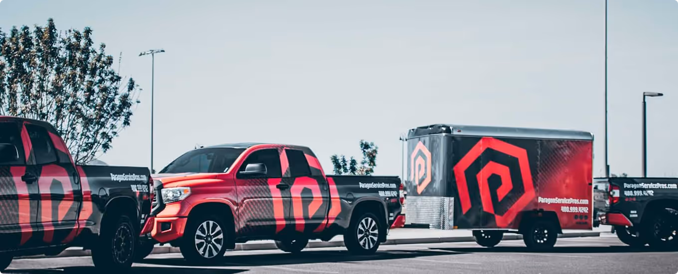 Three black and red pickup trucks and a matching trailer parked outdoors, all branded with a red geometric logo and the website ParagonServicePros.com.