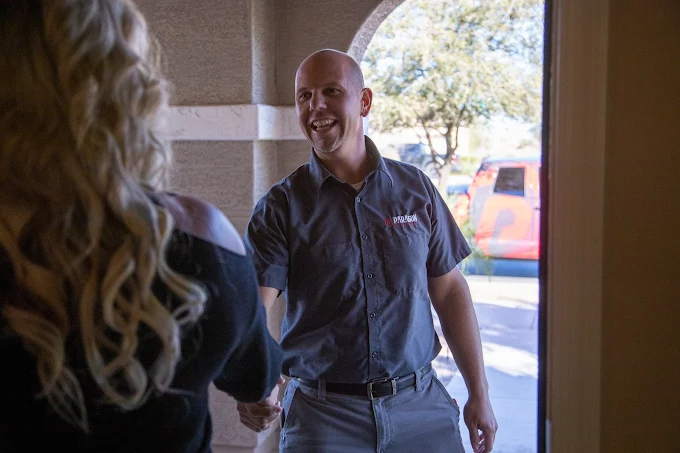 Man in a work shirt smiling and shaking hands with a woman at a doorway.