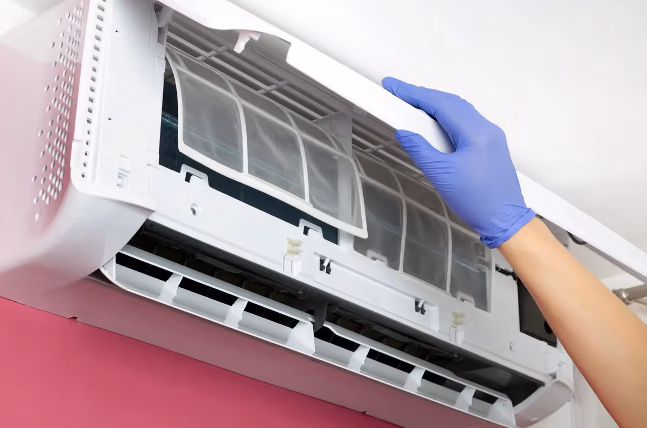 A close-up of a hand in a blue glove replacing the filter in a wall-mounted air conditioner.