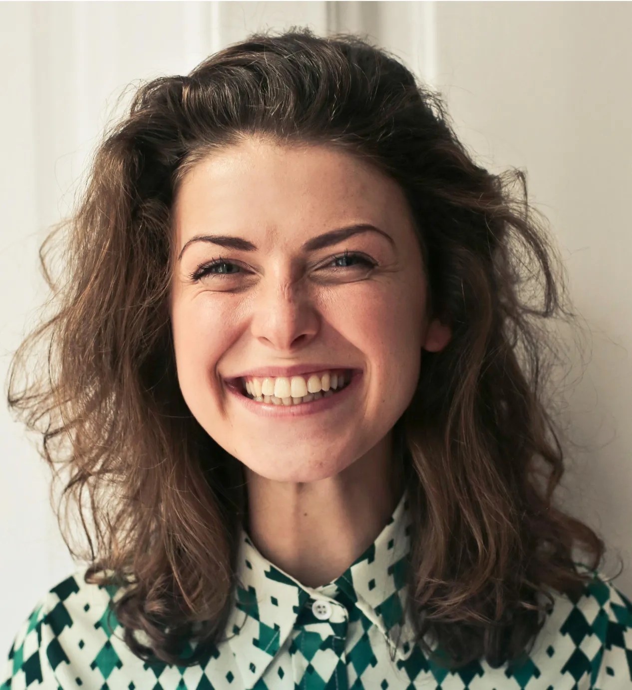 Woman with curly hair smiling brightly in green patterned shirt