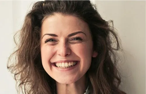Woman with curly hair smiling brightly against neutral background