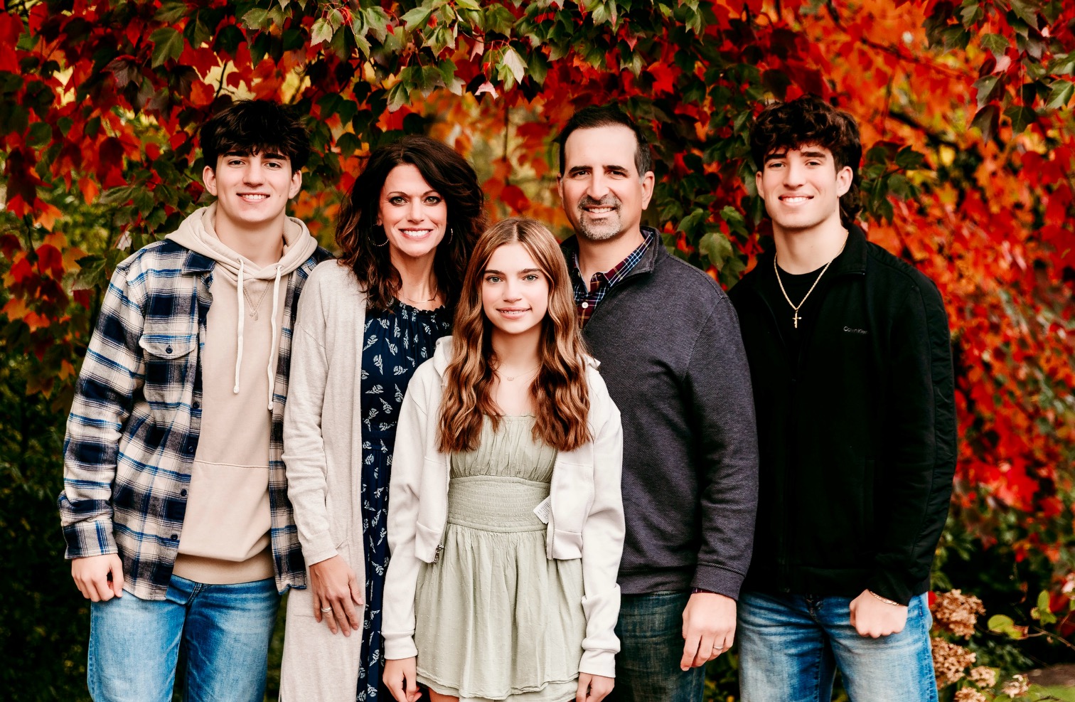 Family of five posing in front of vibrant autumn red and orange leaves