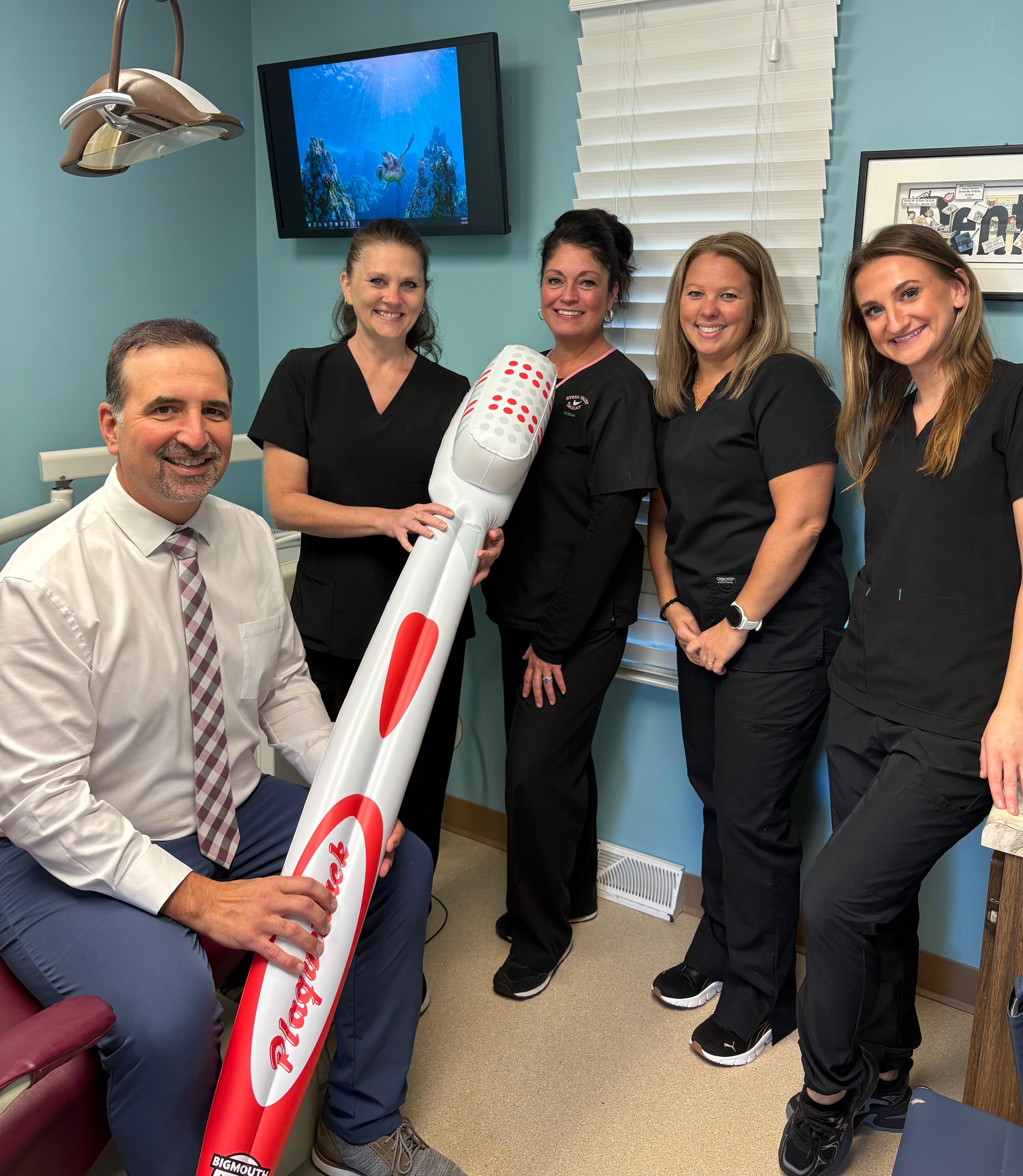 Dental team posing with oversized toothbrush in blue-walled office