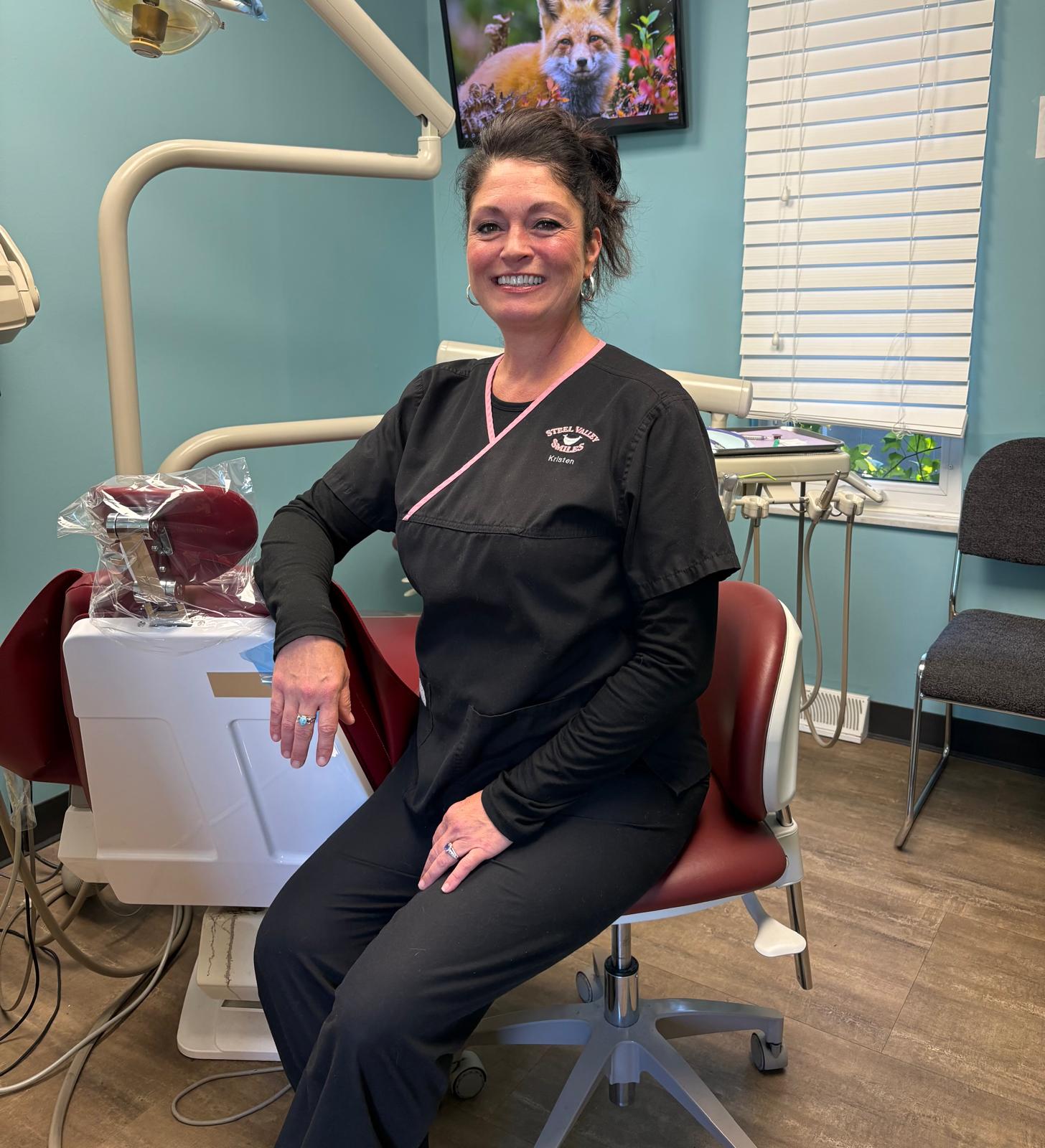 Smiling dental professional in black scrubs sitting in exam room