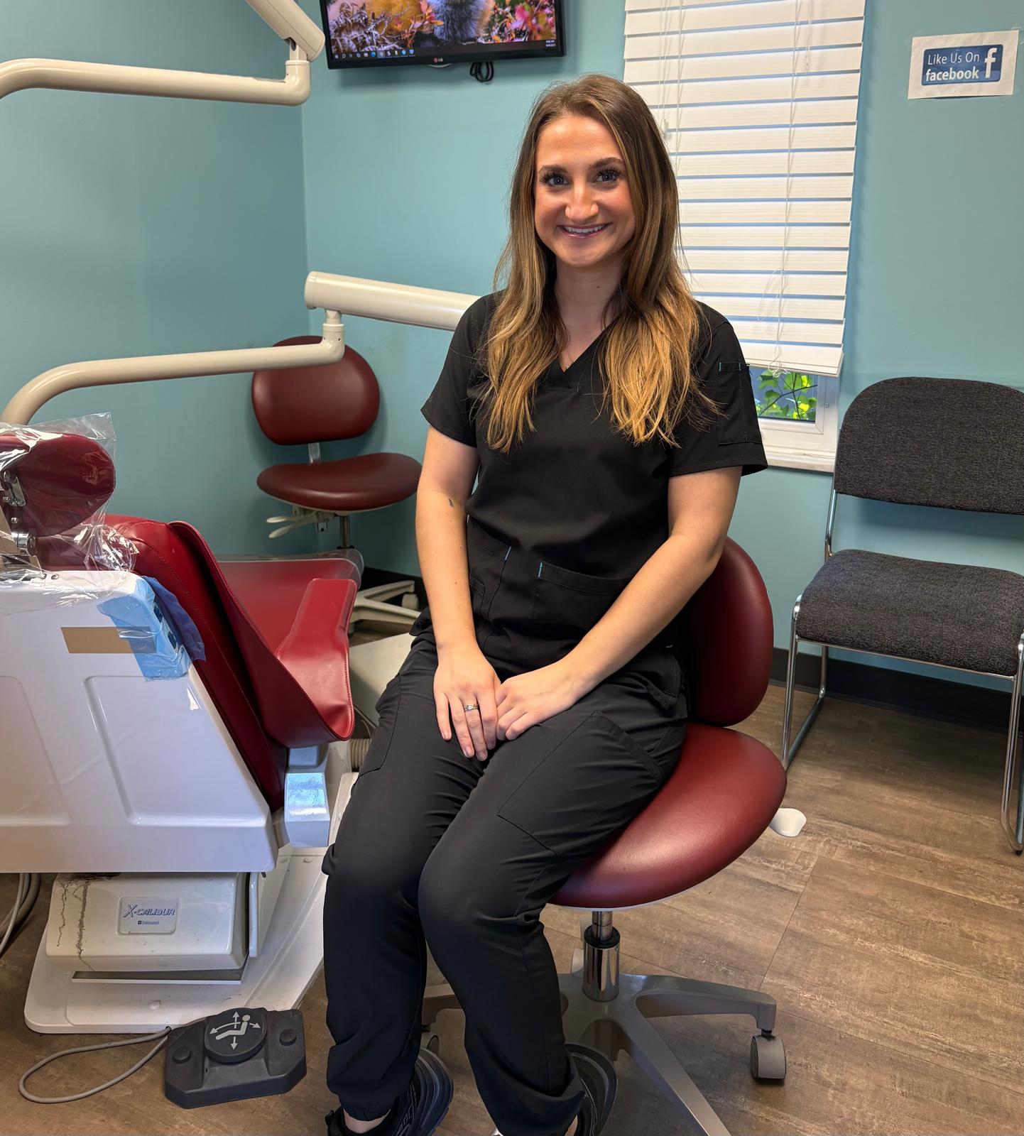 Dental professional in black scrubs sitting in exam room with equipment
