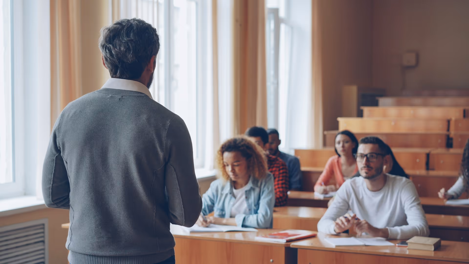 Instructor facing students in a classroom with wooden desks