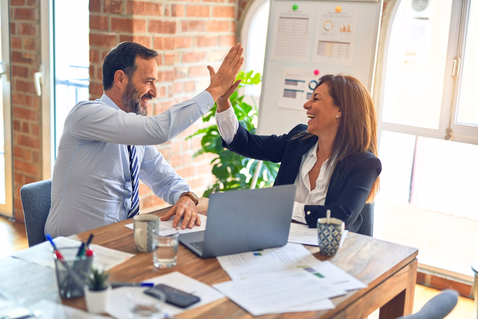 Colleagues high-five and laugh together in bright office workspace
