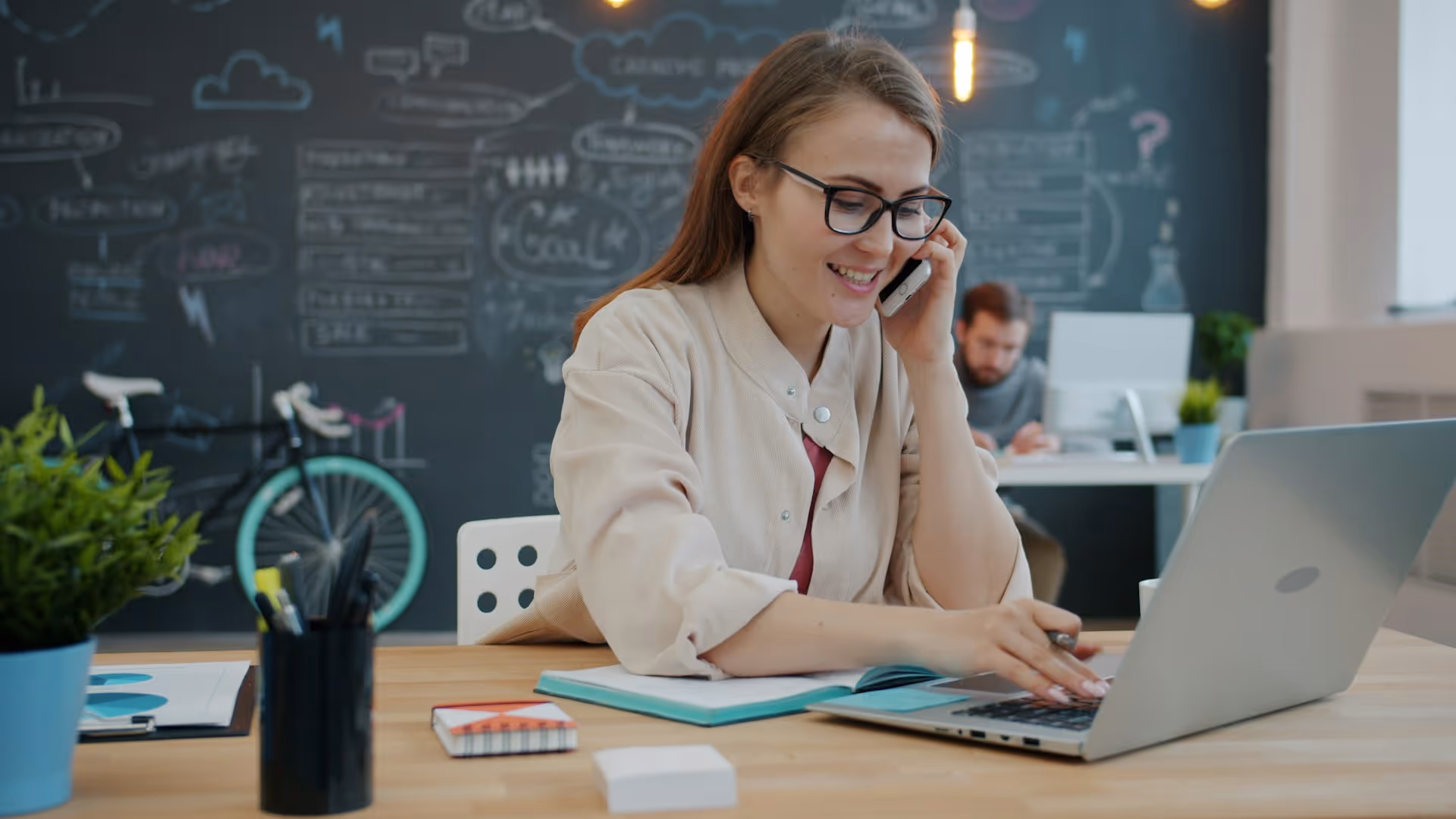 Professional working on laptop while talking on phone in creative office