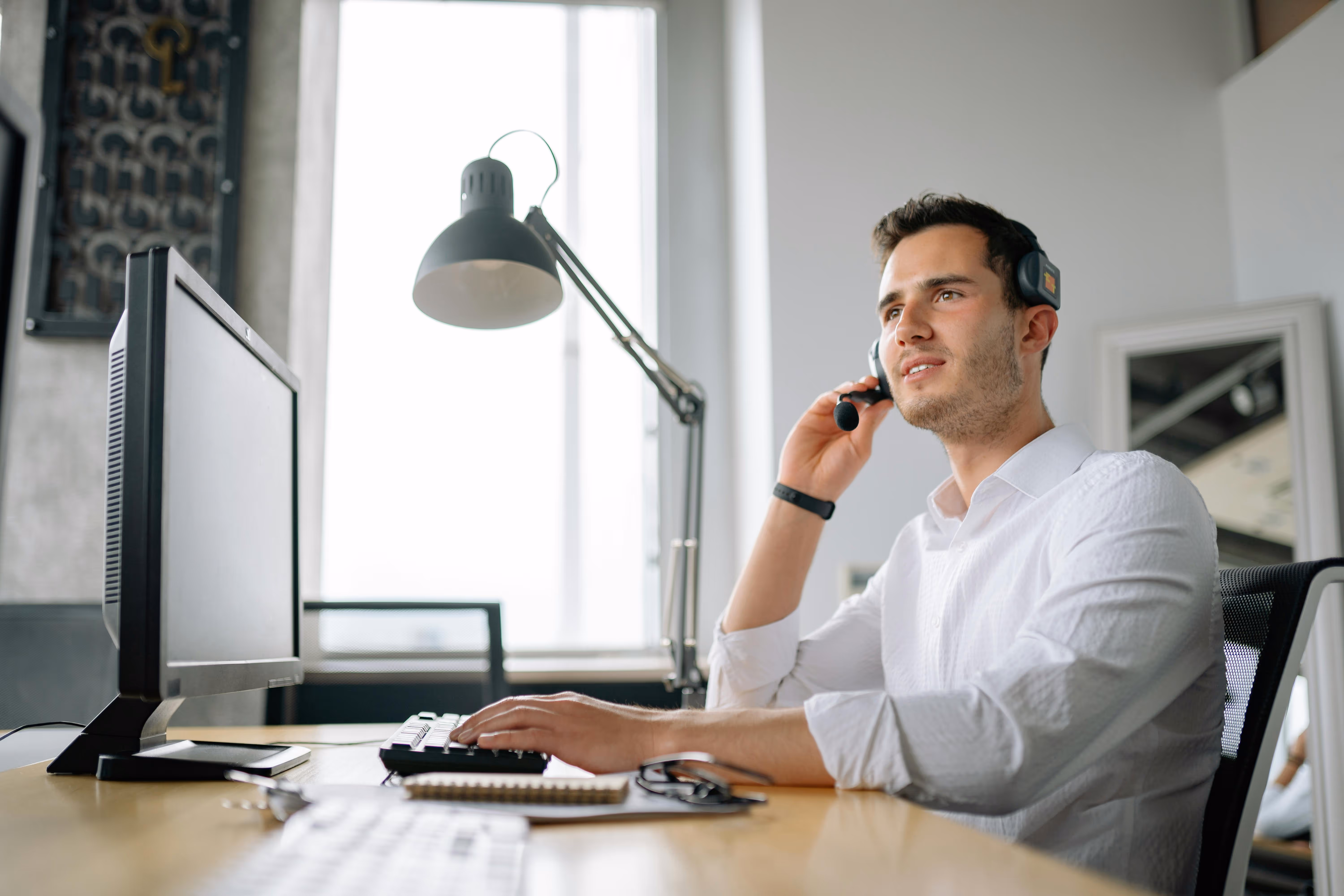 Professional wearing headset works at computer desk with desk lamp