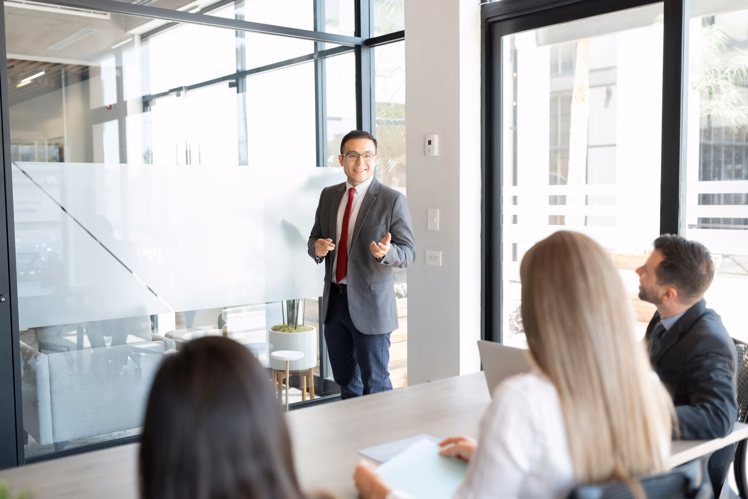 Businessman presenting to colleagues in modern glass-walled conference room