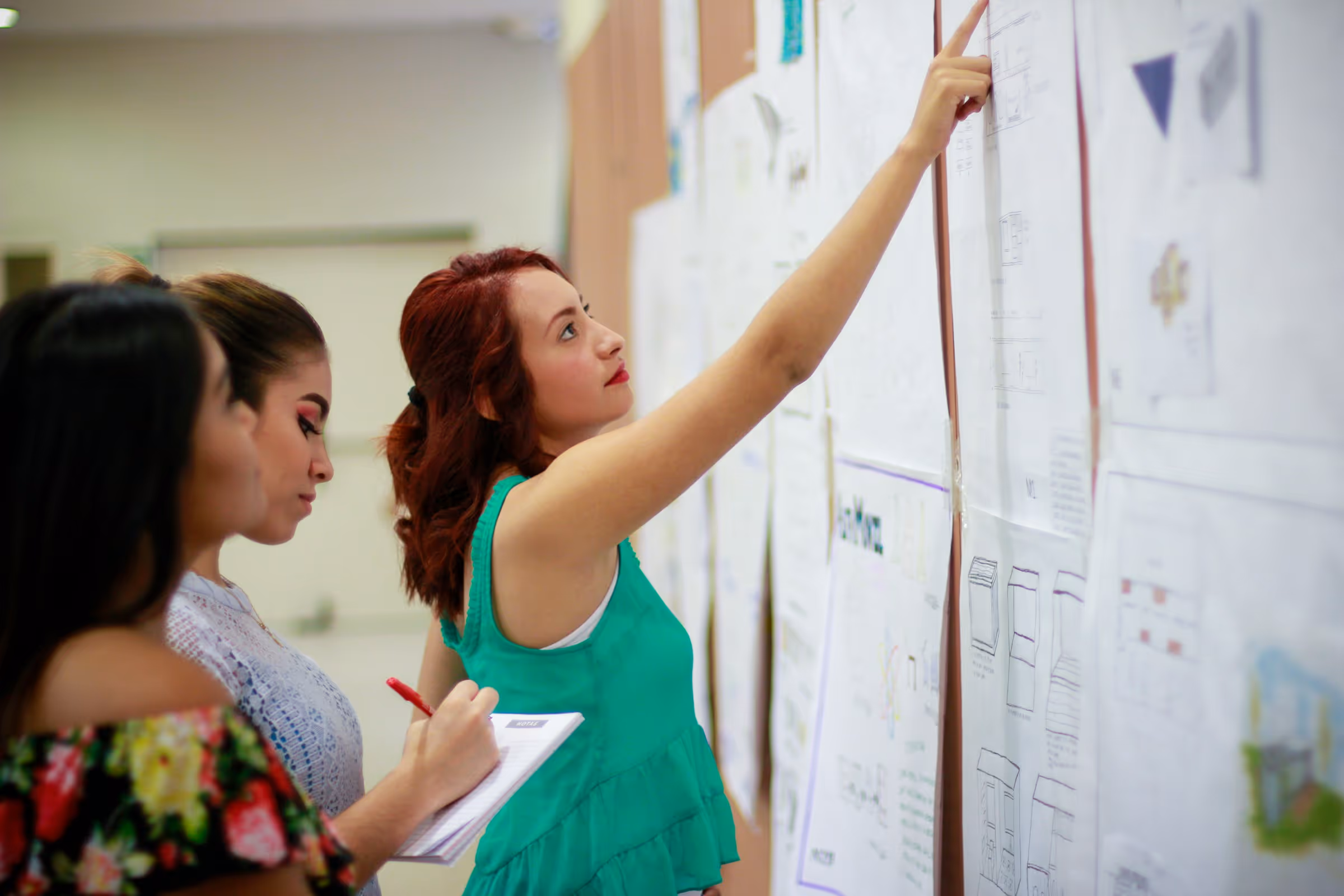 Women collaborating on project, pointing at whiteboard with design sketches