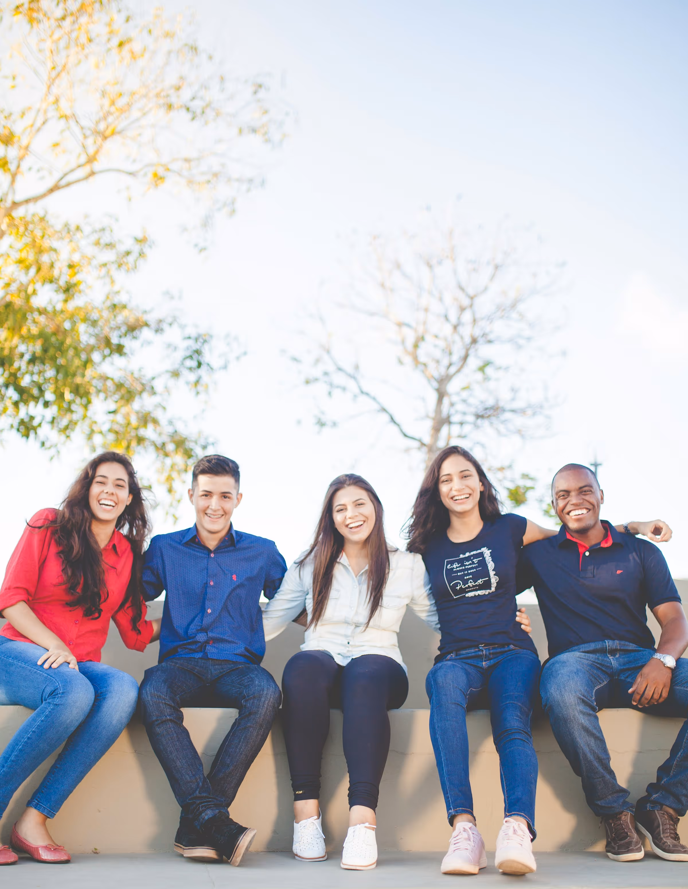 Diverse group of five smiling young people sitting together outdoors