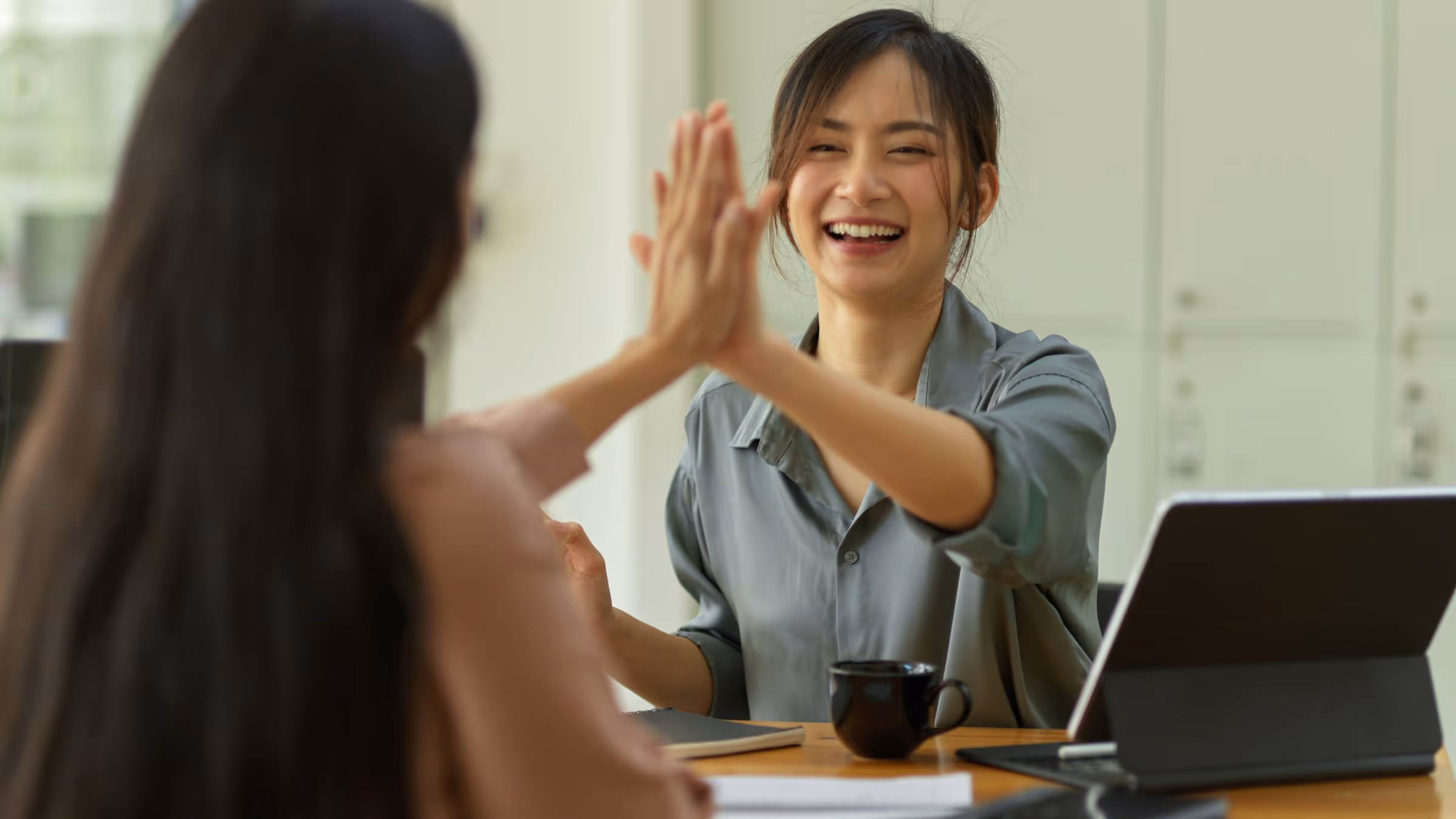 Colleagues giving high-five and smiling at work in bright office