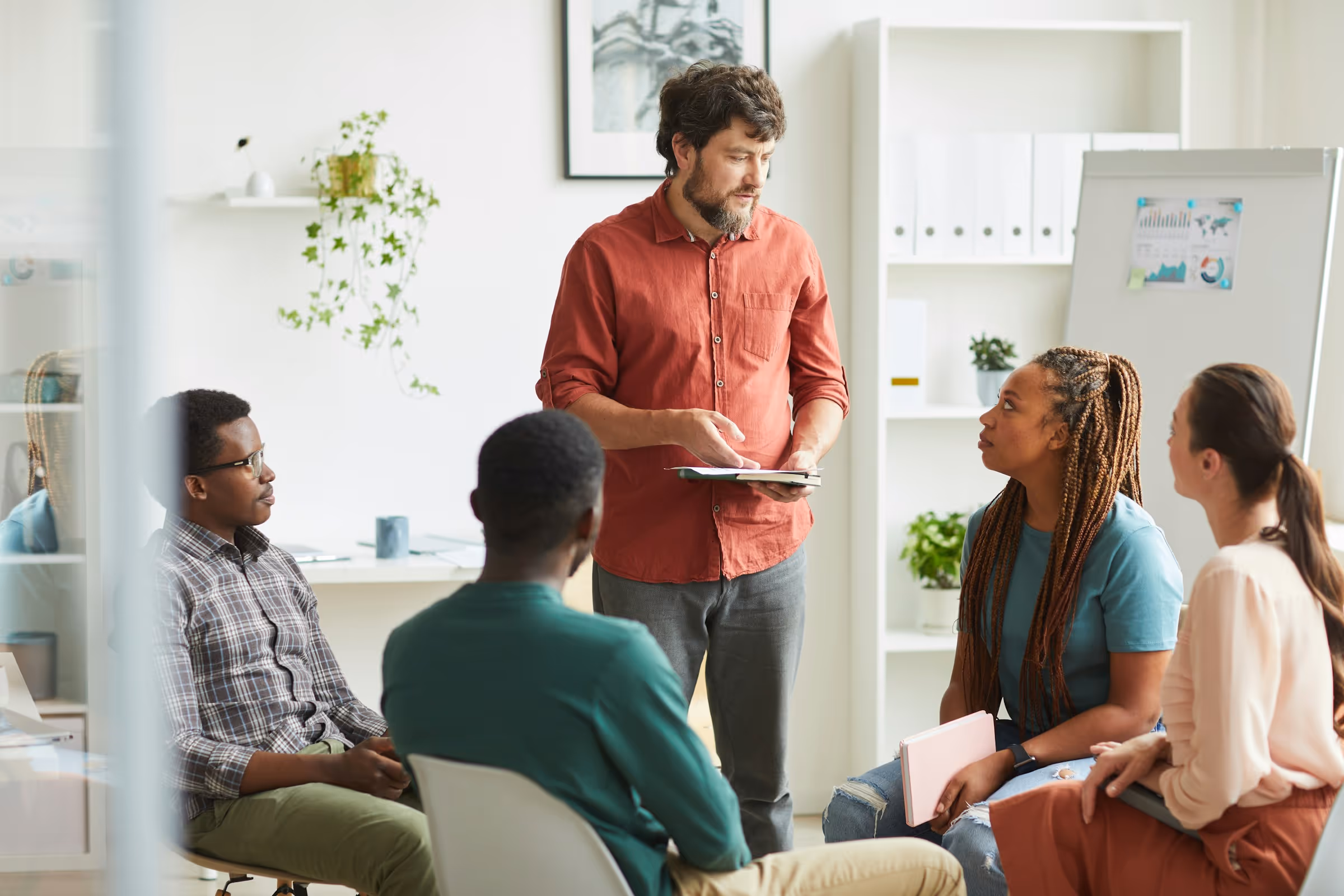 Diverse group in meeting with presenter in red shirt discussing charts
