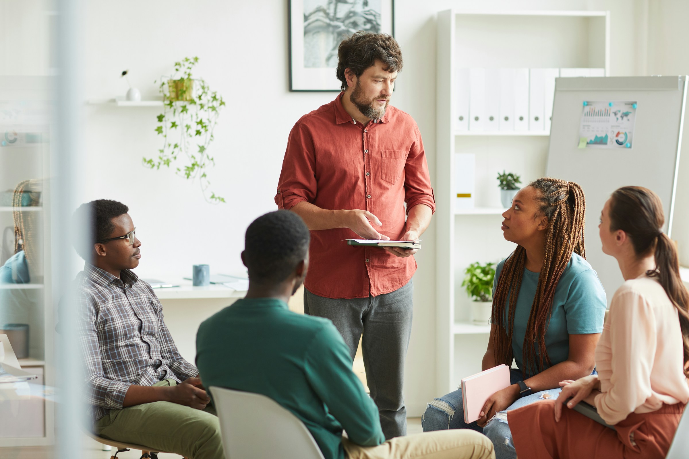 Diverse group in meeting with presenter in red shirt discussing charts