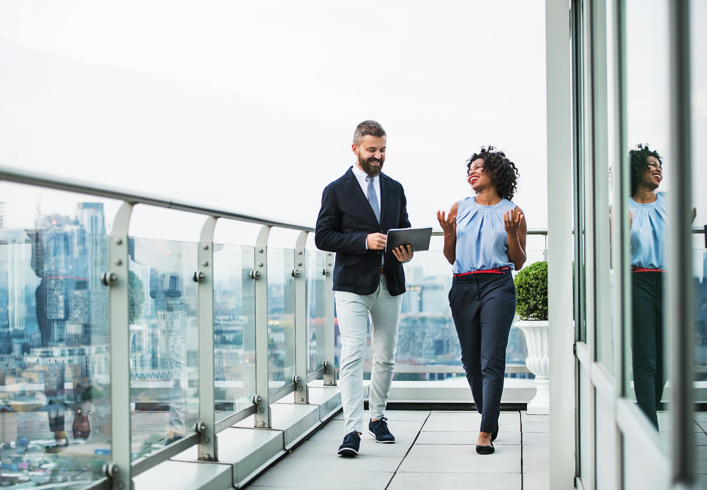 Business colleagues walking and talking on modern office balcony with city view