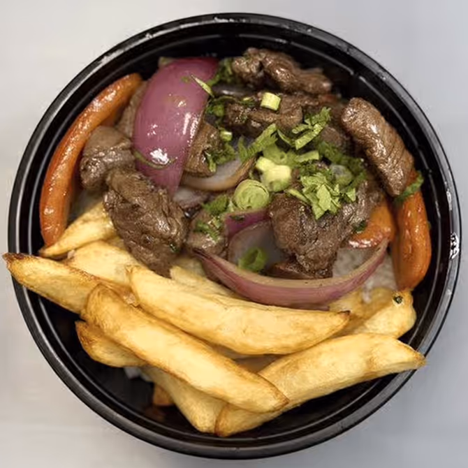 A bowl of flambéed tenderloin with soy sauce, fries, tomatoes, and onions over white rice.