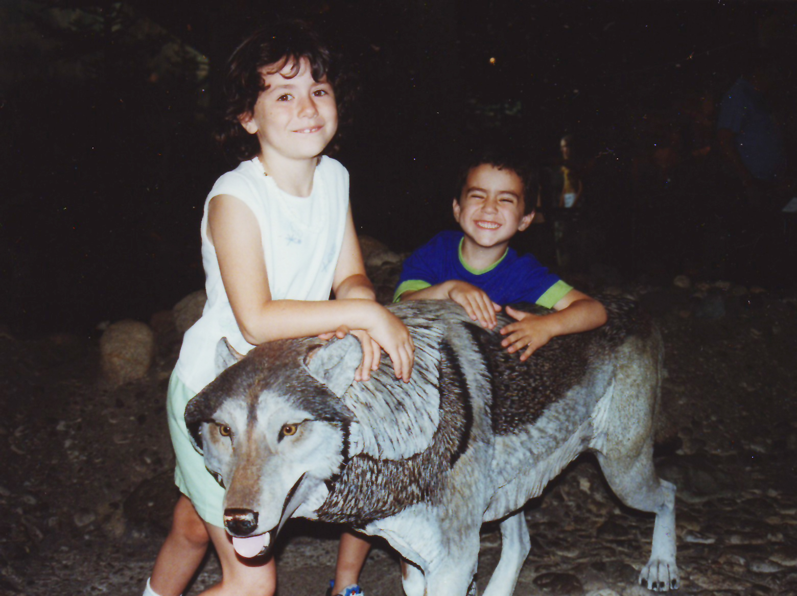 Two smiling children hugging a life-sized wolf statue at night.