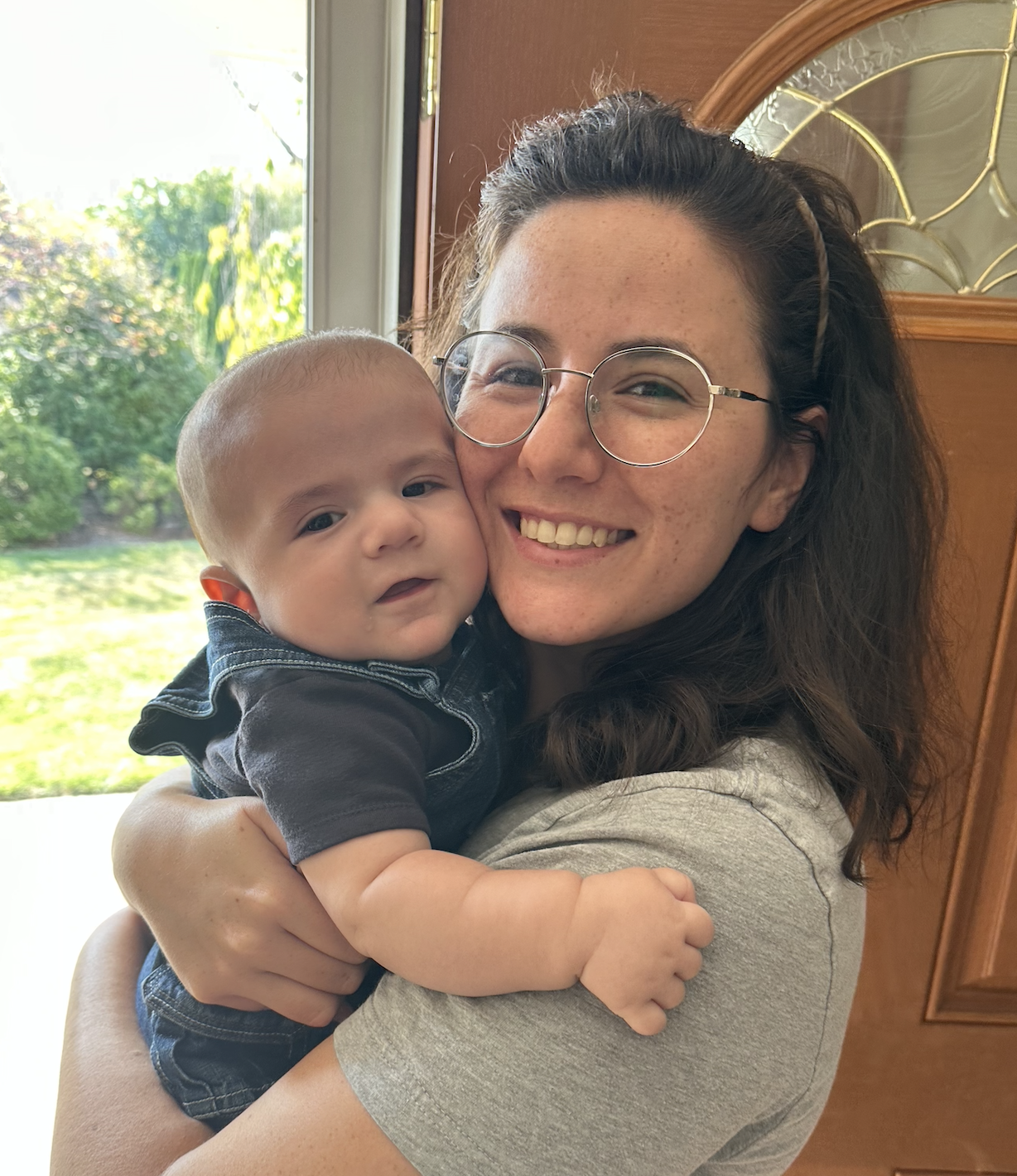 Two children indoors, one wearing glasses smiles in the front while the other behind playfully holds their braided hair out sideways.