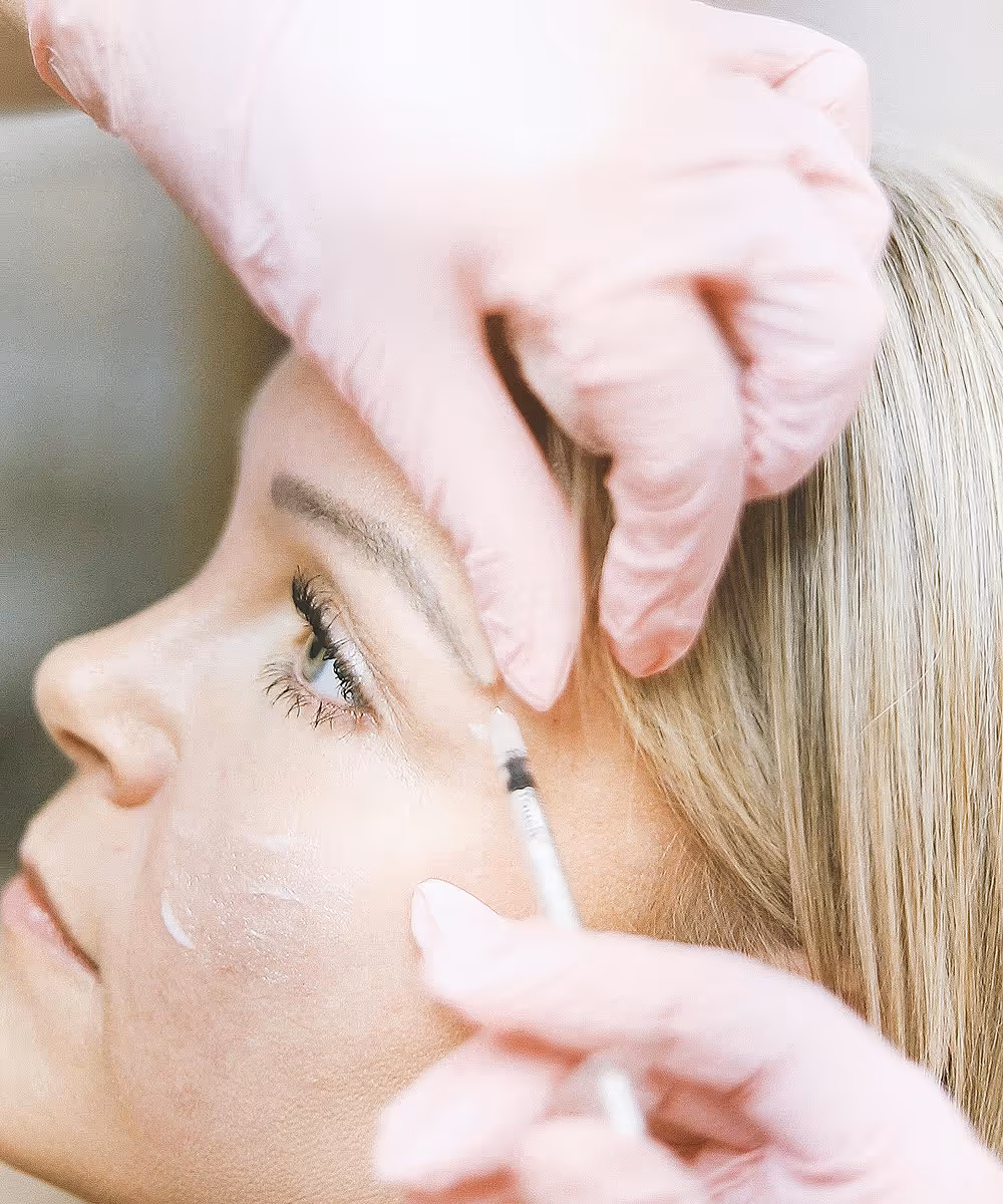Cosmetic injection near the eye area performed by a professional wearing pink gloves.