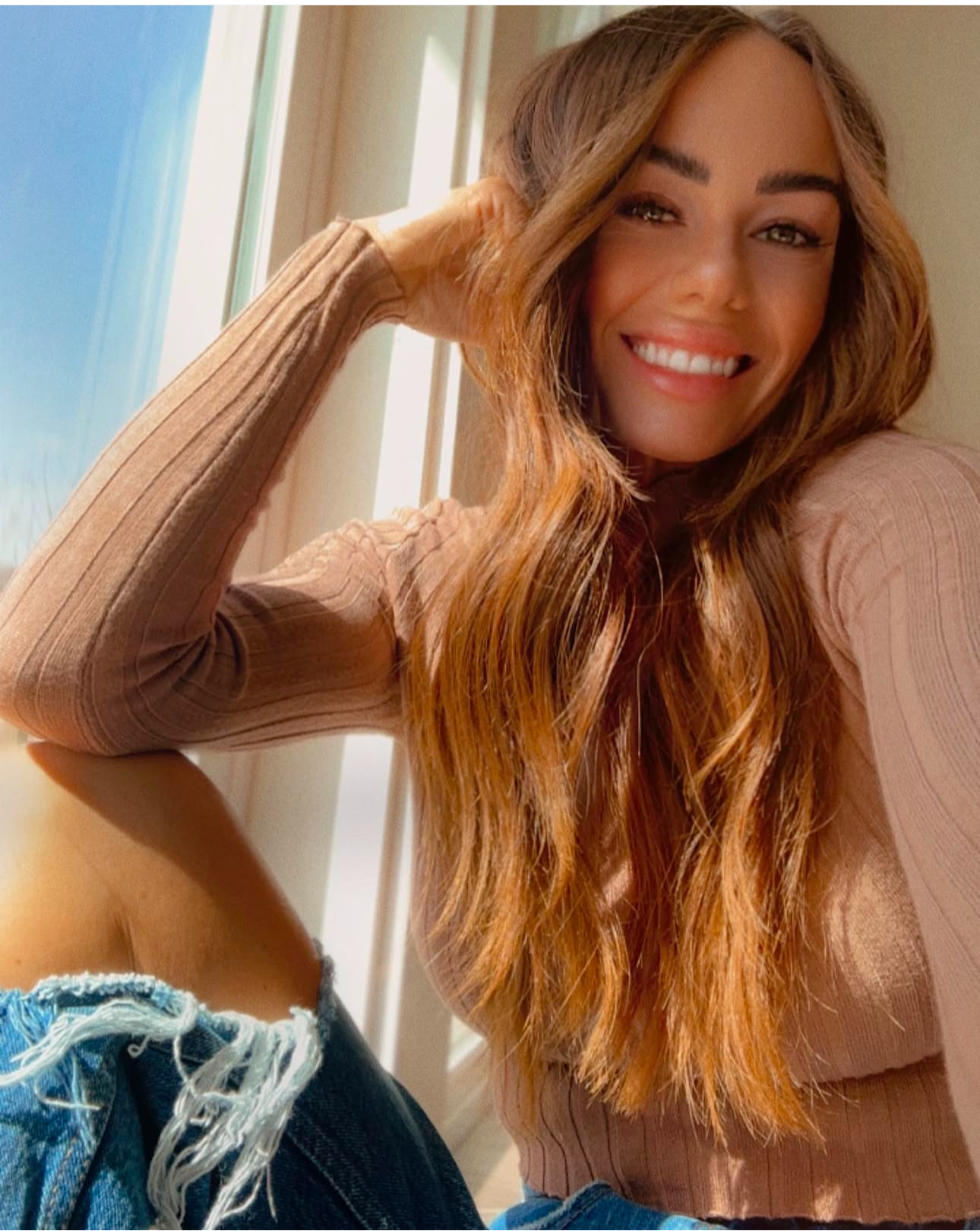 Woman with short dark hair and tattooed arm sitting on a white chair, smiling slightly.