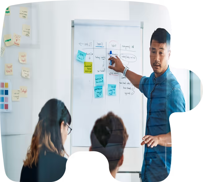 Man in blue shirt presenting a project plan on a whiteboard to two seated colleagues.