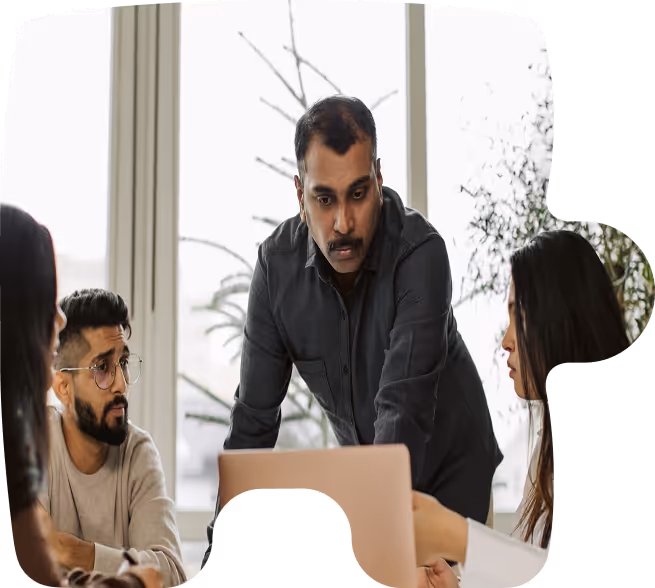 Four colleagues in a meeting with one standing and explaining something on a laptop while others listen attentively.