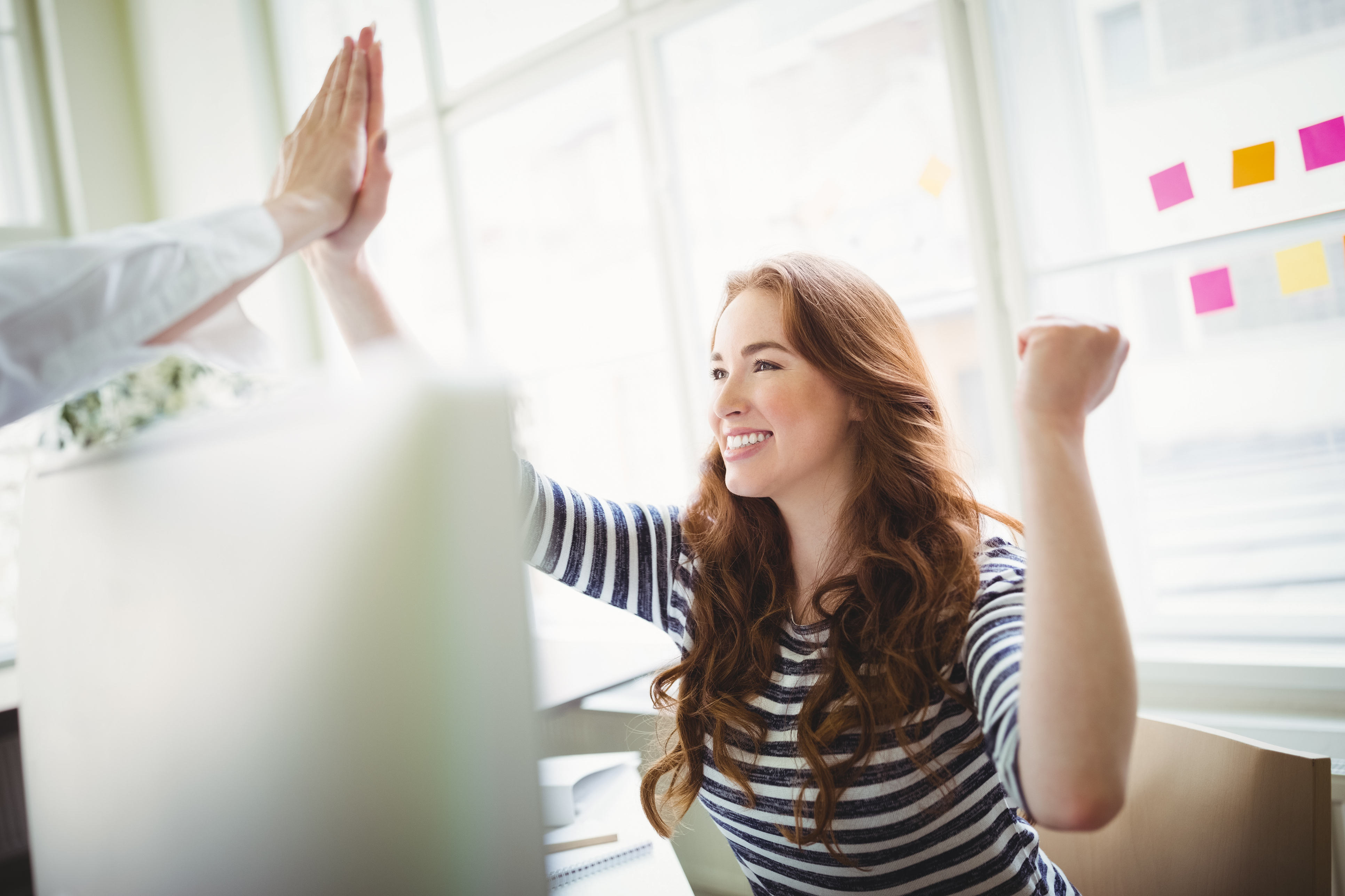 Excited coworkers giving high-five at desk in creative office