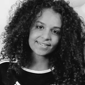Smiling young woman with curly hair wearing a dark top with white trim.