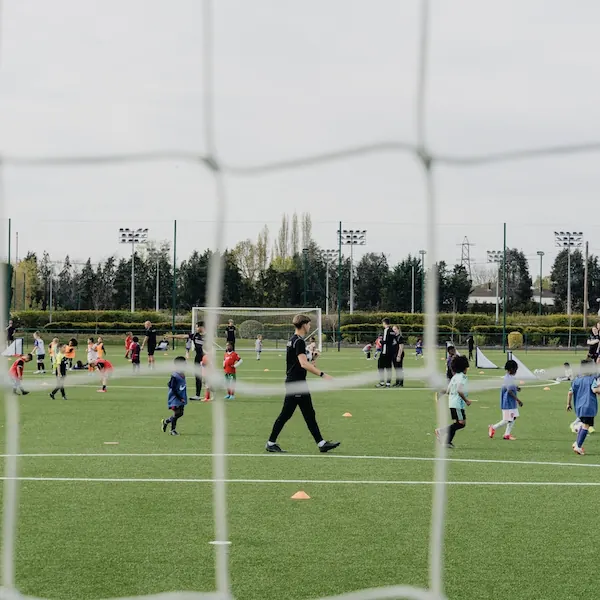 Children playing soccer on a green field with coaches guiding them, viewed through a soccer goal net.