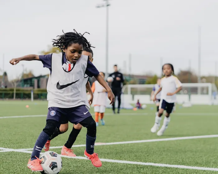 Young boys playing soccer on a green field with a coach in the background.