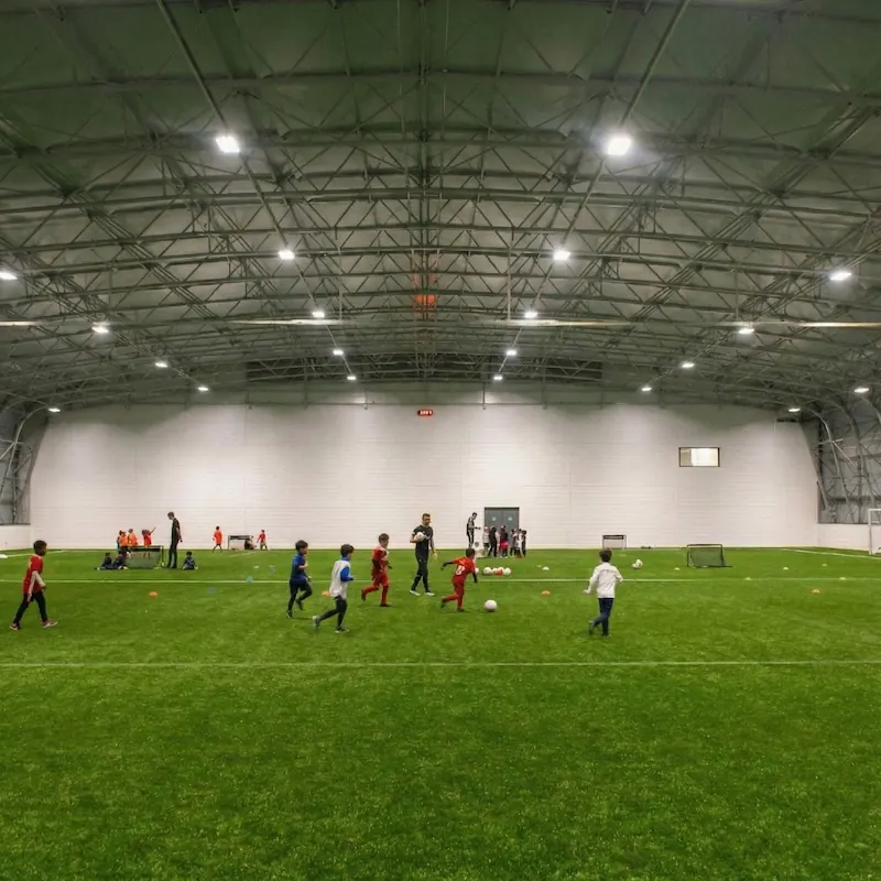 Children playing soccer inside a large, well-lit indoor sports facility with artificial turf.