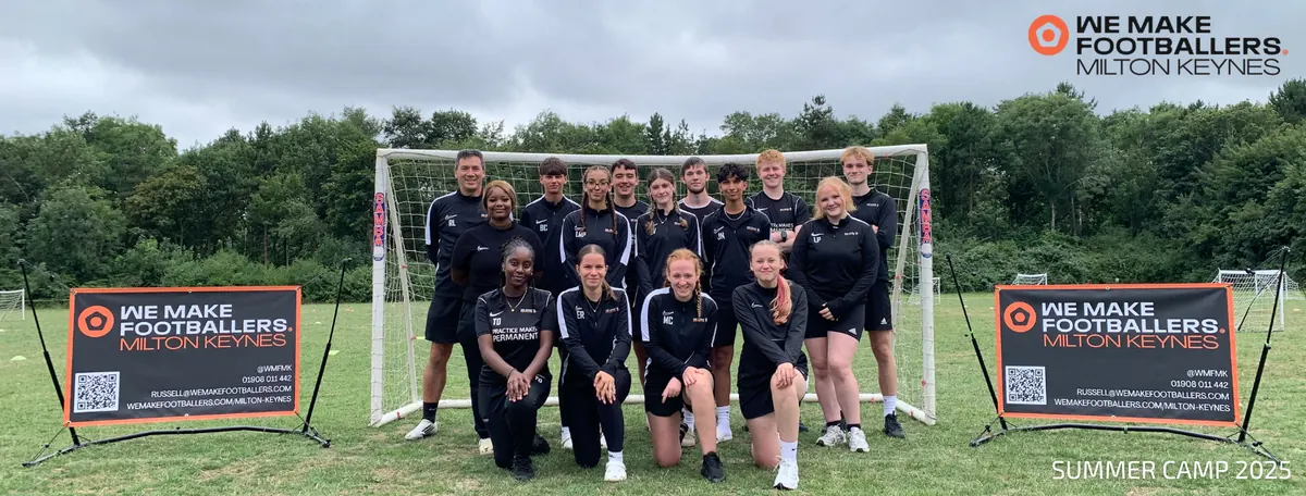Group photo of a mixed-gender football team posing in front of a goal on a grassy field with two promotional banners for We Make Footballers Milton Keynes and the text Summer Camp 2025.