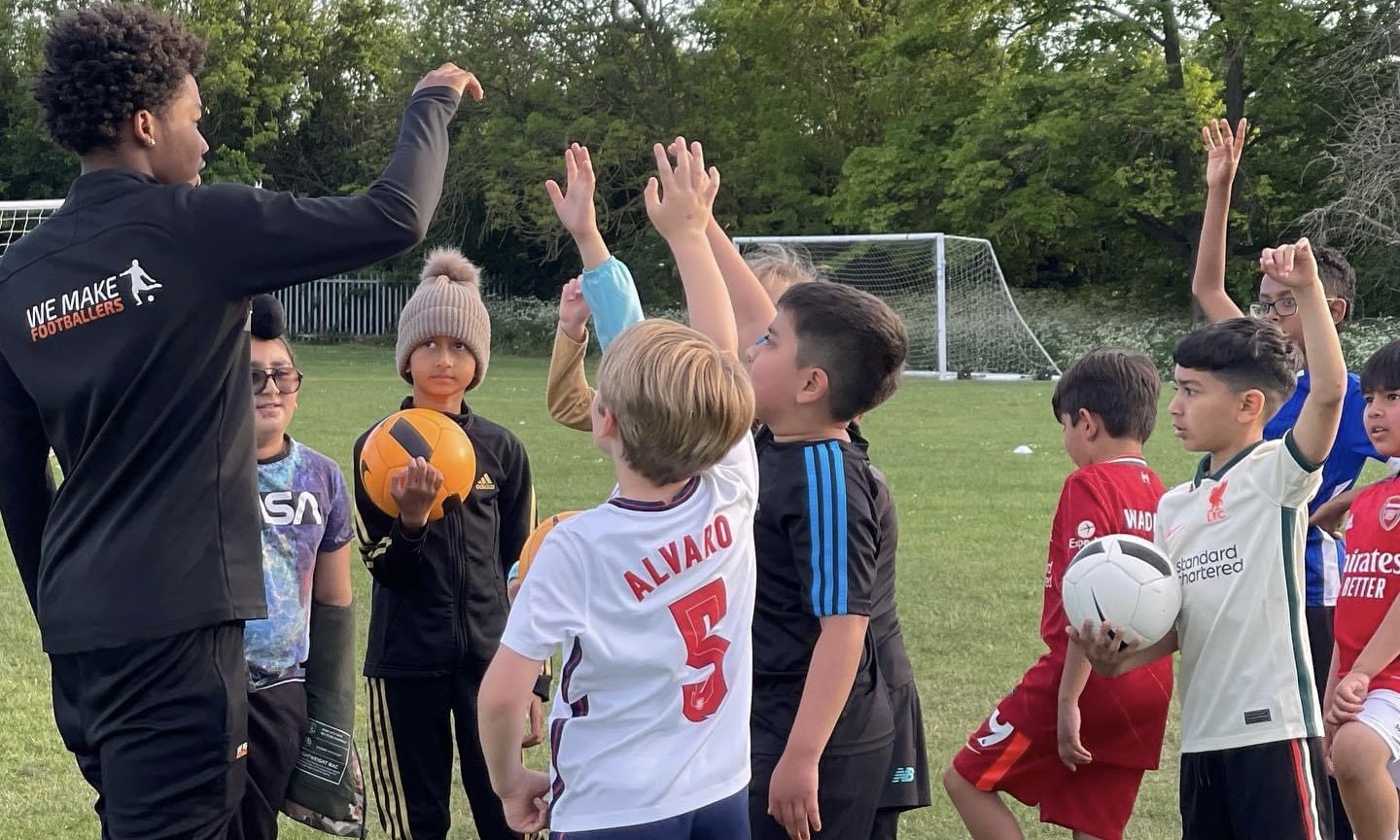 Coach high-fiving children holding footballs