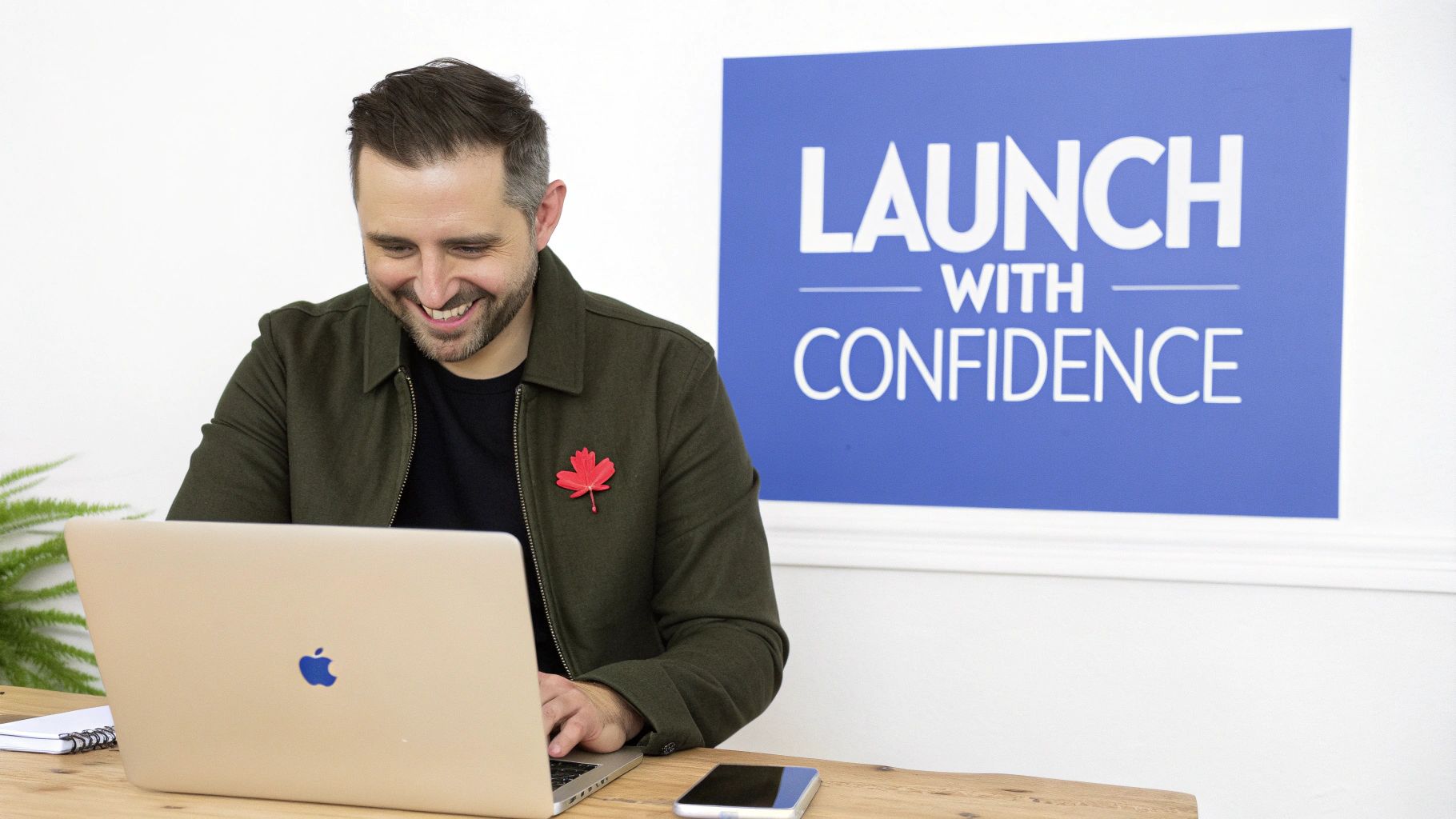 Smiling man with a maple leaf pin works on a laptop, a 'Launch With Confidence' sign behind him.